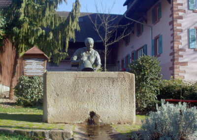 Der Buchbrunnen beim Zieglerhof (2001). Errichtet im Jahre 1996. Die Sandsteinfigur wurde wegen Schäden im August 2003 mit einer Bronzefigur ausgetauscht.