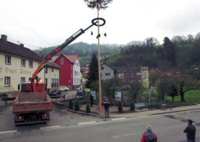Der Maibaum 2021 wird mit einem Lastwagen-Kran in der Dorfmitte in die Senkrechte gestellt.