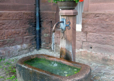 Der Sandsteinbrunnen an der Südwest-Ecke des alten Schulhauses. Es ist einzige öffentliche Brunnen im Ort, der fast ausnahmslos das ganze Jahr über Wasser führt.