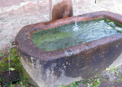 Der Sandsteinbrunnen an der Südwest-Ecke des alten Schulhauses. Es ist einzige öffentliche Brunnen im Ort, der fast ausnahmslos das ganze Jahr über Wasser führt.