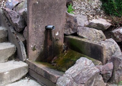 Der Sandsteinbrunnen im Pfarrgarten befindet sich am barrierefreien Zugang zum Pfarrsaal unterhalb des Pfarrzentrums.