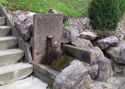 Der Sandsteinbrunnen im Pfarrgarten befindet sich am barrierefreien Zugang zum Pfarrsaal unterhalb des Pfarrzentrums.