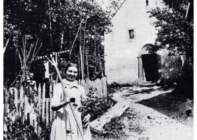 Die Dreifaltigkeitskapelle mit Mesnerin Appolonia Ohnemus im Vordergrund. Das kleine Kirchlein wurde 1922 zugunsten einer größeren Kirche abgerissen.