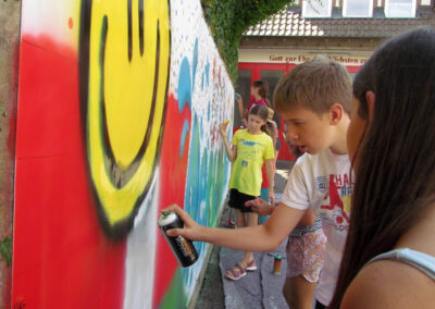 Momentaufnahmen von der Graffiti-Aktion der Dörlinbacher Jugend bei der Alten Schule. 15 Jugendliche eine triste Stützmauer in ein leuchtendes Wandbild.