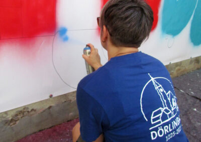 Momentaufnahmen von der Graffiti-Aktion der Dörlinbacher Jugend bei der Alten Schule. 15 Jugendliche eine triste Stützmauer in ein leuchtendes Wandbild.