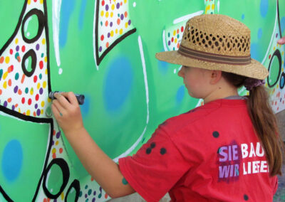 Momentaufnahmen von der Graffiti-Aktion der Dörlinbacher Jugend bei der Alten Schule. 15 Jugendliche eine triste Stützmauer in ein leuchtendes Wandbild.